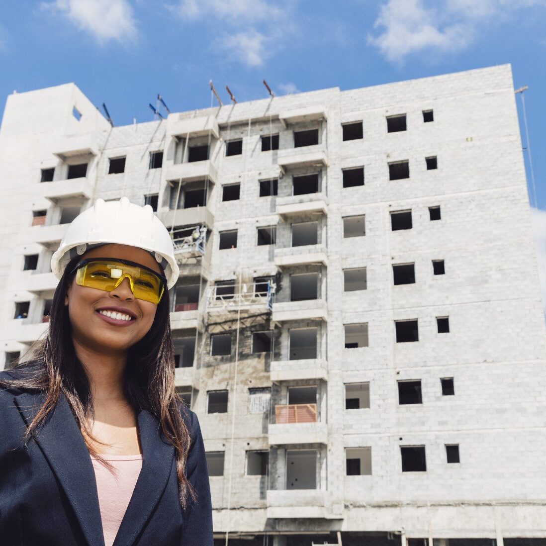 A woman wearing a hard hat standing in front of a building under construction.